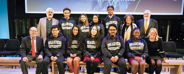 Two rows of people in Brandeis sweatshirts smile for the camera